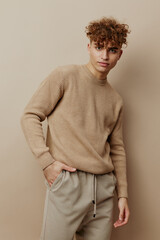 a handsome, attractive man in stylish clothes stands on a beige background and poses relaxed with his hands in his pockets, looking at the camera