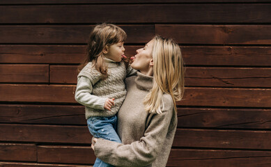 A young mother holding a little daughter in her arms, mother and baby stick out tongues.