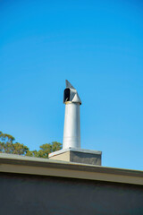 Obraz premium Metal gray chimney pipe on top of flat building with roof gutters on flat top and dark stucco exterior with background foliage