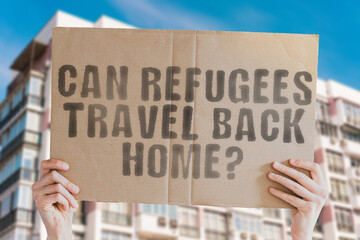 The question " Can refugees travel back home? " is on a banner in men's hands with blurred background. Freedom. War. Ethnic. Government. Human. Liberty. Right. Immigrant. Migration. Regime. Arrest