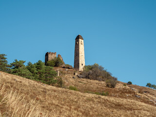Sunny afternoon in the Caucasus mountains. noon in the Caucasus mountains. Medieval tower on autumn mountain slope background. Ingushetia region.