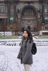 Fototapeta premium Young female tourist walking in the park in front of the Berlin Cathedral with snow all over the ground.