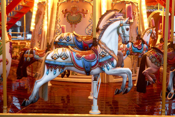 Old French carousel roundabout, galloper with illumination at an amusement in a holiday park. Horse on a traditional fairground vintage carousel. Merry-go-round. Outdoor vintage colorful luminous.