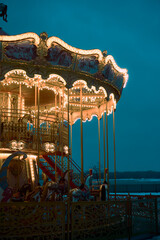 Children's Carousel roundabout, galloper at an amusement park in the evening at night illumination. Outdoor vintage colorful luminous. Blue background. New year, christmas entertainment mood concept.