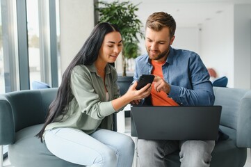 Smiling businesspeople work collaborate on computer, brainstorm over company startup at office meeting. Motivated diverse colleagues look at laptop screen discuss business project ideas together