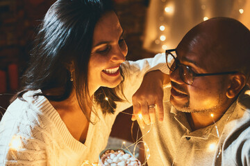 Happy interracial couple celebrating New Year at home together, sitting garland close to each other