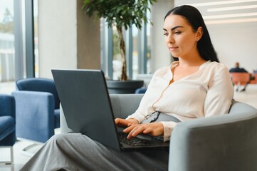 Young business woman sitting at sofa and working with laptop at the waiting hall of the business...