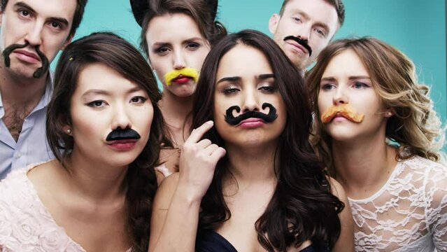 People, prop and photobooth at party with friends for birthday, holiday or social event celebration with funny group in studio. Men and women together in booth with moustache to celebrate birthday