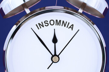 insomnia word or text between clock hands on a face of chrome retro alarm clock isolated on blue background. sleep disorder concept