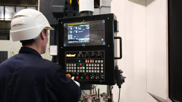 A male worker in a construction helmet works with a computer, a robot in a factory in white gloves. The builder checks the computer program at the factory. High quality 4k footage.