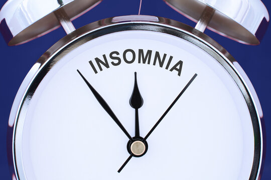 insomnia word or text between clock hands on a face of chrome retro alarm clock isolated on blue background. sleep disorder concept