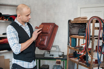 the craftsman in the workshop examines the finished leather product - a hand-made briefcase bag