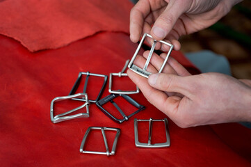 a selection of decorative metal buckles. Craftsman hands and metal buckles top view on red leather background. Accessories for sewing clothes.