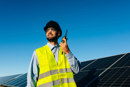 Worker with walkie talkie near solar panels in daylight