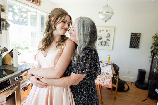 Affectionate Mother Hugging Teenage Daughter In Prom Dress At Home