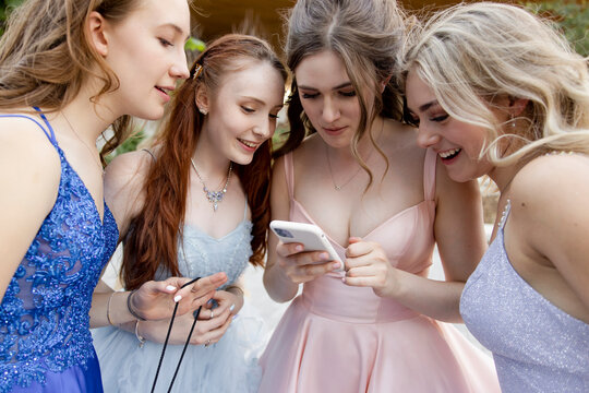 Teenage Girl Friends In Prom Dresses Using Smart Phone