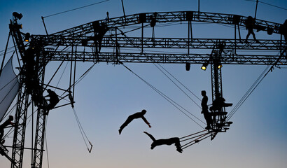 silhouettes of trapeze artists acrobats on the metal scaffolding at sunset - obrazy, fototapety, plakaty