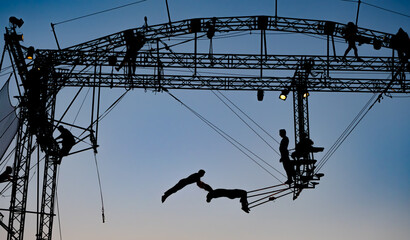 silhouettes of trapeze artists acrobats on the metal scaffolding at sunset