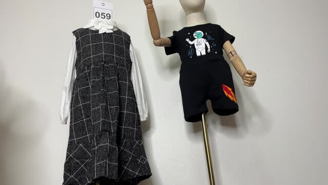 Child mannequin wear shirt, pants and dress on gold pole holding number card with white wall background