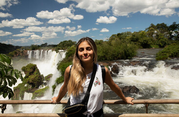 Tourism. Portrait of a young woman with brown hair smiling with the Iguazu waterfalls in the...