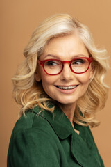 Closeup portrait of beautiful smiling middle aged woman wearing stylish eyeglasses looking away. Confident mature fashion model with curly blonde hair posing for pictures isolated on background  