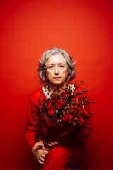 Portrait of a senior woman wearing red clothes, holding a red roses bouquet, over a red background