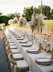 Stylish wedding banquet with decorative dry flowers in beige colors, cutlery and crystal on background of landscape in countryside
