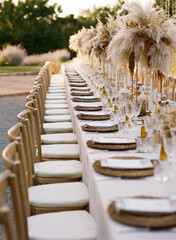 Front view of stylish decoration of wedding festive table with dried flowers and straw plates on background of field in countryside