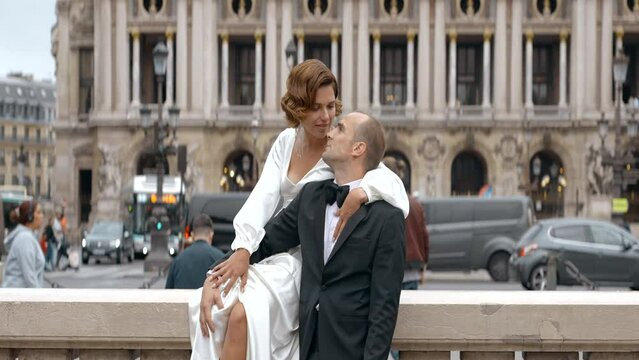 Loving couple video shooting on their wedding day. Action. Bride in white dress and groom in suit on the background of big city architecture.