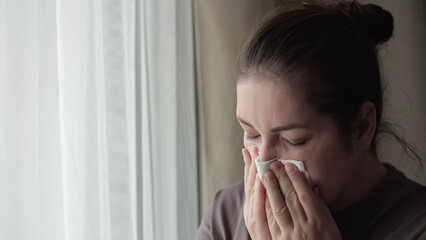 Sick brunette woman sneezes covering nose with napkin feeling unwell. Housewife tries to handle...
