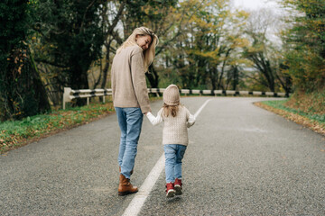 Rear view of a mother walking along a rural road with her little daughter.