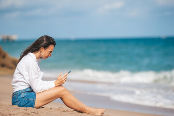 Fototapeta na wymiar Young woman using mobile phone on the beach. Girl texting in a smartphone on the seashore