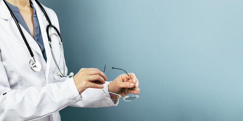 Hands of female doctor ophthalmologist or optician holds pair of glasses. Minimal blue background. Copy space. Optics oculist, eye test checkups. Medicine mockup template