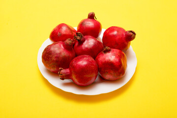 Seven ripe red pomegranates on a white plate on a yellow background