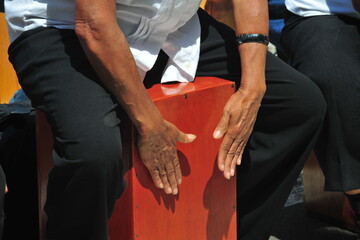 Close-up of a cajon, man's legs and hands are shown as he's playing the instrument in the square of...