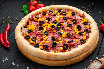 Tasty and big pizza with different types of meat. Pizza with sausage, ham, corn and olives.