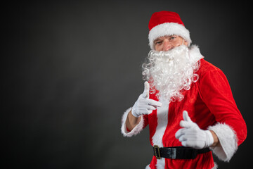 Fototapeta na wymiar Portrait von einem verkleideten Weihnachtsmann der auf einen Platzhalter zeigt und isoliert vor grauen Hintergrund ist 
