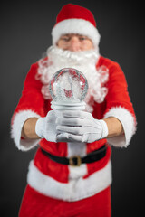 
Portrait von einem verkleideten Weihnachtsmann mit einer Schneekugel in der Hand vor grauen Hintergrund 