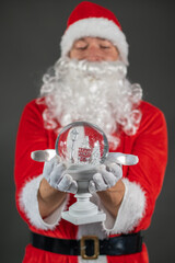 
Portrait von einem verkleideten Weihnachtsmann mit einer Schneekugel in der Hand vor grauen Hintergrund 