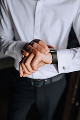 A man, a businessman in a white shirt holds a smartwatch, a wristwatch on his hand, preparing in the morning. Photography, business.