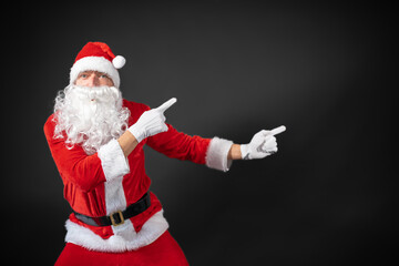 Portrait vom Weihnachtsmann der auf einen Platzhalter zeigt und isoliert vor grauen Hintergrund ist 