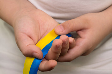 A girl in a white T-shirt holds a yellow-blue ribbon (the State flag of Ukraine) in her hands. Close-up