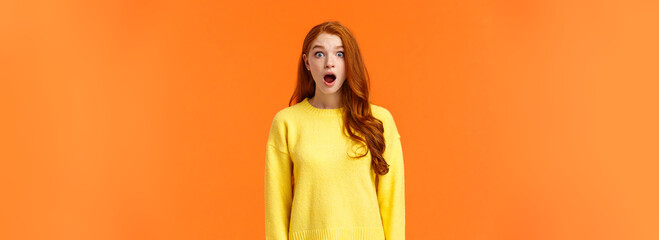Shocked redhead cute girl drop jaw astounded and speechless, stare camera popped eyes, cant...