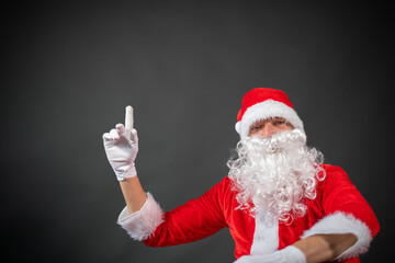 Portrait vom Weihnachtsmann der auf einen Platzhalter zeigt und isoliert vor grauen Hintergrund ist 