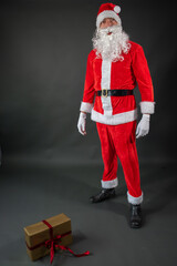 
Portrait von einem verkleideten Weihnachtsmann mit einem Geschenk in der Hand vor grauen Hintergrund 