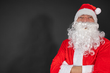 Portrait von einem verkleideten Weihnachtsmann mit einem Geschenk in der Hand vor grauen Hintergrund 