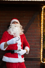 Portrait von einem verkleideten Weihnachtsmann, der auf einem Weihnachtsmarkt von Lichtern umgeben...