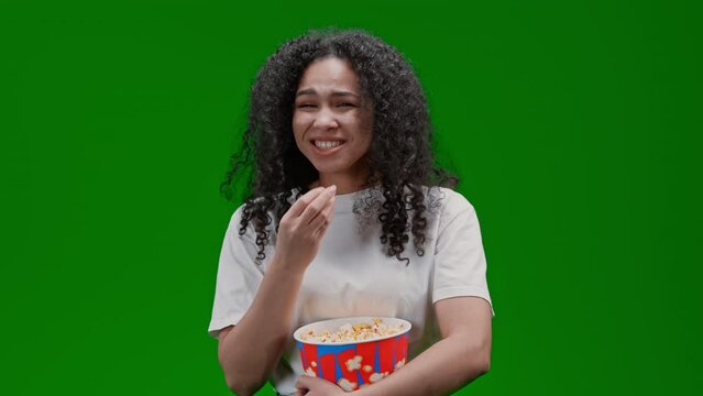 overjoyed woman with curly long hair dressed white tee eating popcorn watching comedy movie laughing Isolated on Green Screen