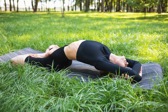 Young woman leading a healthy lifestyle and practicing yoga, doing Matsyasana exercise, fish pose, exercising alone on a summer morning in the park on a mat