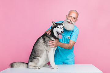 Full size photo of satisfied good mood doctor wear blue uniform pet husky sitting on table checkup isolated on pink color background